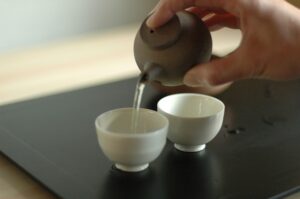 A hand pours tea from a Japanese teapot into small bowls