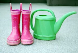 Pink rain boots sit next to a green watering can
