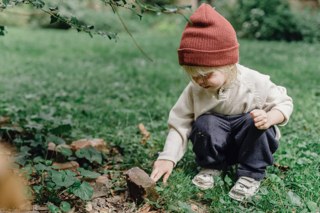 Young child outdoors looks at a rock